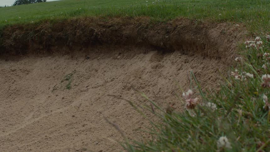 A golf ball rolls down into a sand trap bunker in slow motion on a golf course