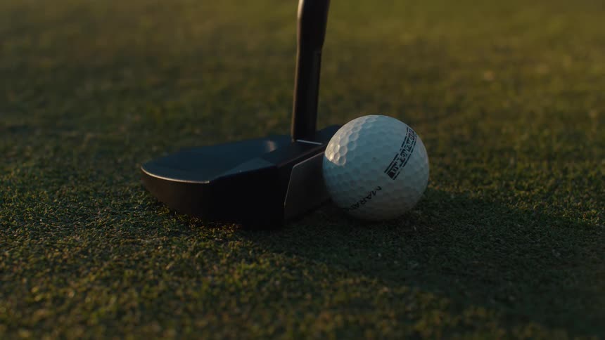 In a dramatic slow-motion close-up, a golf putter strikes a ball on a perfectly manicured green