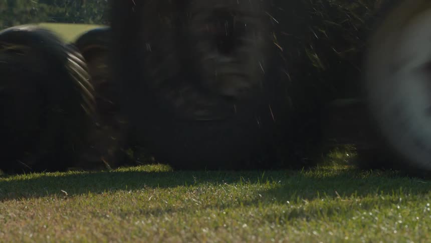 A low-angle shot of a large gang reel mower cutting the lush green grass on a golf course on a sunny day