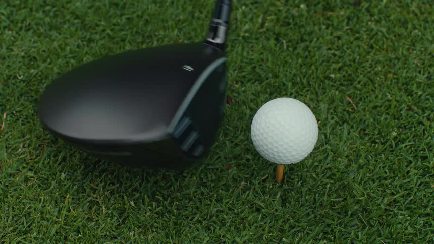 Slow-motion close-up of a driver hitting a golf ball off a tee on a green lawn