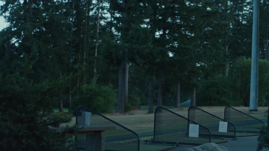 Sprinklers water the green at a quiet, empty golf driving range surrounded by trees at dusk