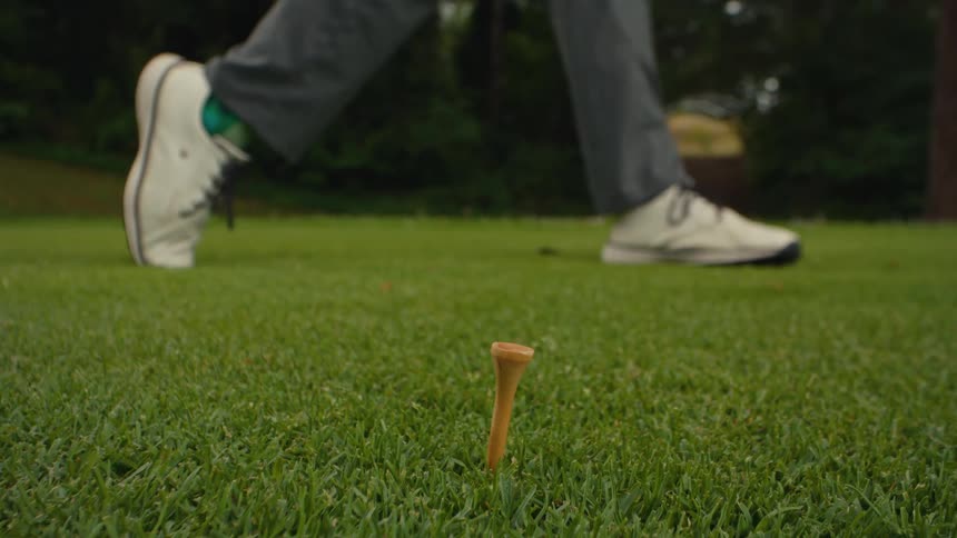 Extreme close-up in slow motion of a golf driver striking a ball off a tee, after which the golfer retrieves the tee