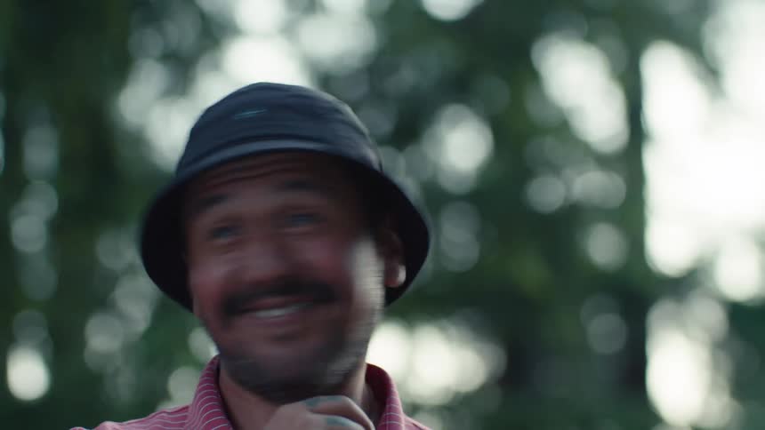 Candid close-up of a man in a bucket hat laughing and smiling while having a conversation outdoors