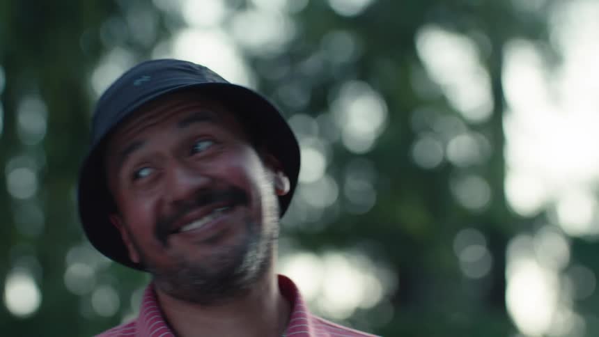 A close-up portrait of a joyful man in a bucket hat turning and smiling while enjoying a day outside