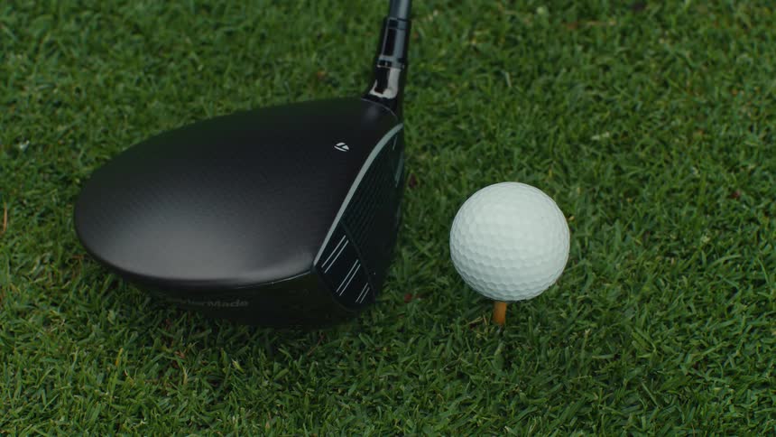 A close-up, slow-motion shot of a golf driver hitting a ball off a tee on a lush green course