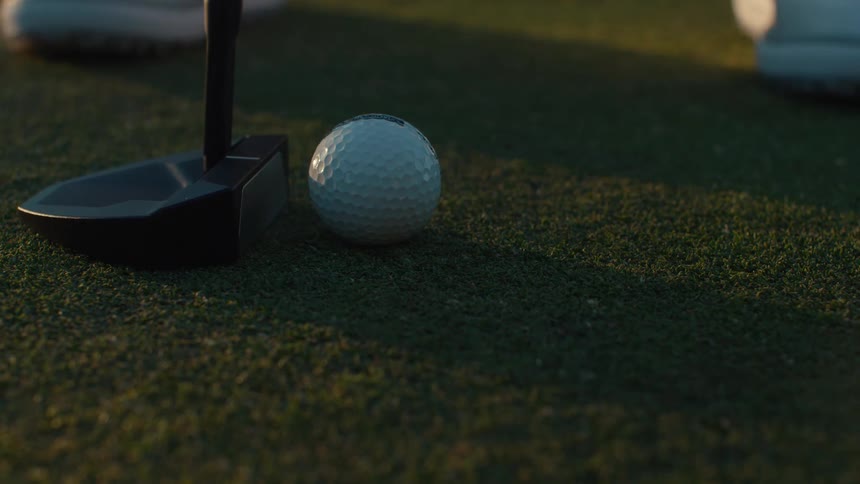 A golfer places a golf ball on the green and putts it away in slow motion during a sunny afternoon game