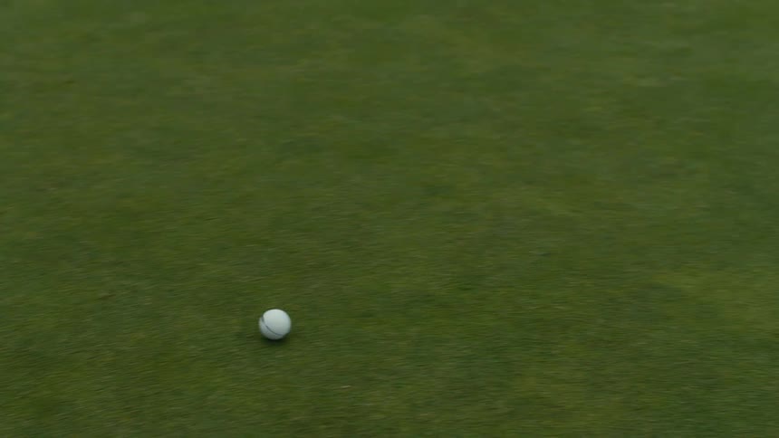 A close-up high-angle shot follows a golf ball as it rolls across a putting green