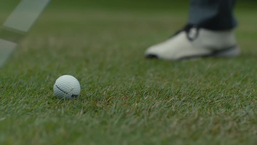 Close-up slow motion of a golfer striking a golf ball with an iron, sending grass flying