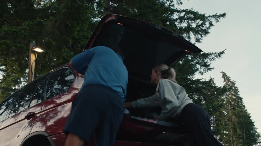A man and woman in slow motion take their golf bags out of the back of a red SUV at a golf course