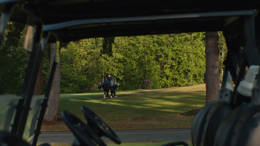 View from inside a golf cart of people walking with their clubs on a beautiful, green golf course on a sunny day