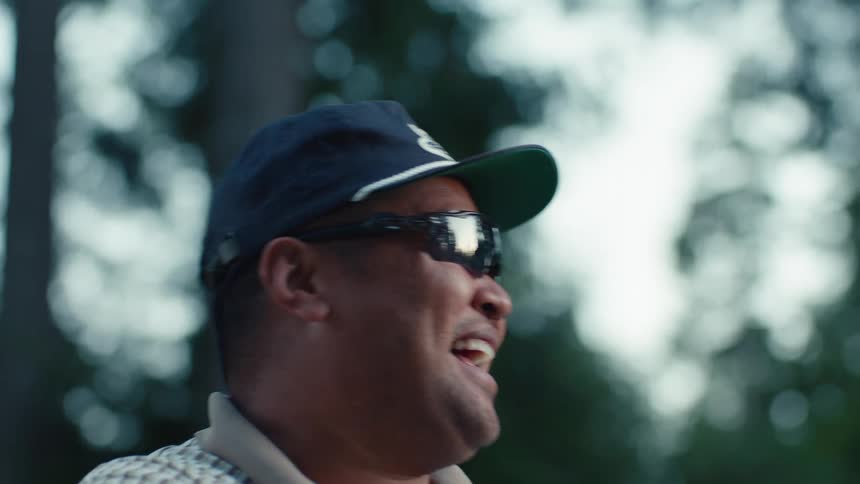 Slow motion close up of a man in sunglasses and a hat laughing after being surprised