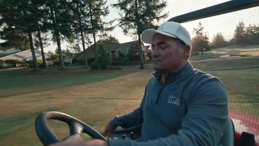 A man drives a utility vehicle across a serene golf course during a beautiful sunrise