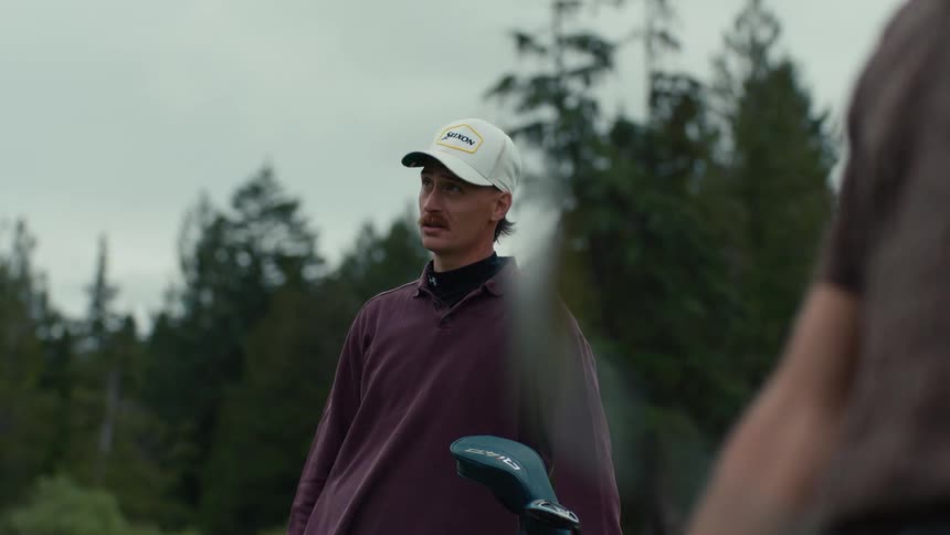 A man in a baseball cap watches his friend's slow-motion golf swing and then offers some friendly advice on the lush green course