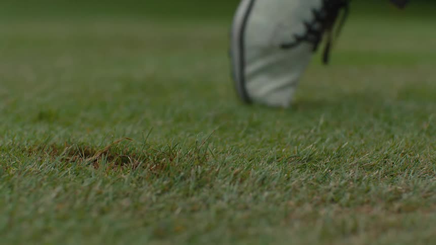 Slow motion close-up of a golf iron striking a golf ball on a lush green fairway, taking a divot