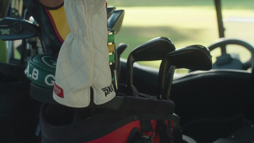 A close-up of a golfer selecting a golf club from a red and black bag in a golf cart