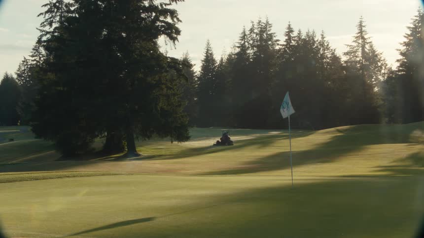 View through binoculars of a groundskeeper mowing the grass on a sunny, picturesque golf course