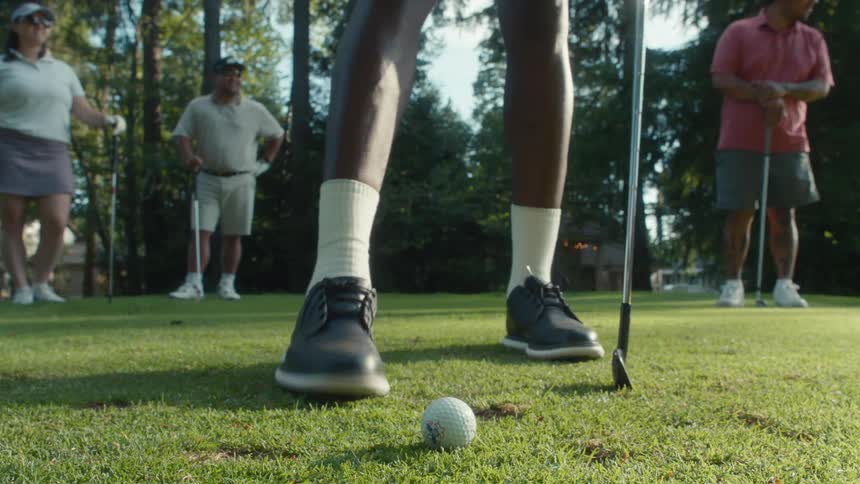 Slow motion low angle shot of a golfer teeing off while friends watch in the background on a sunny day