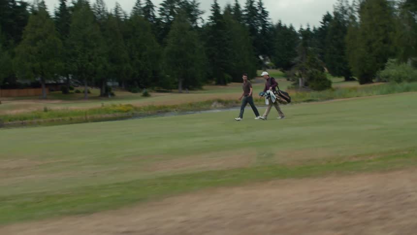 Side-tracking shot of two men walking together across a lush green golf course fairway