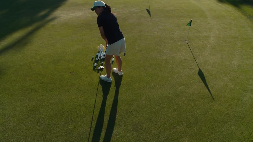 High angle shot of a female golfer practicing putting on a sunlit green, emptying a basket of balls for her training session
