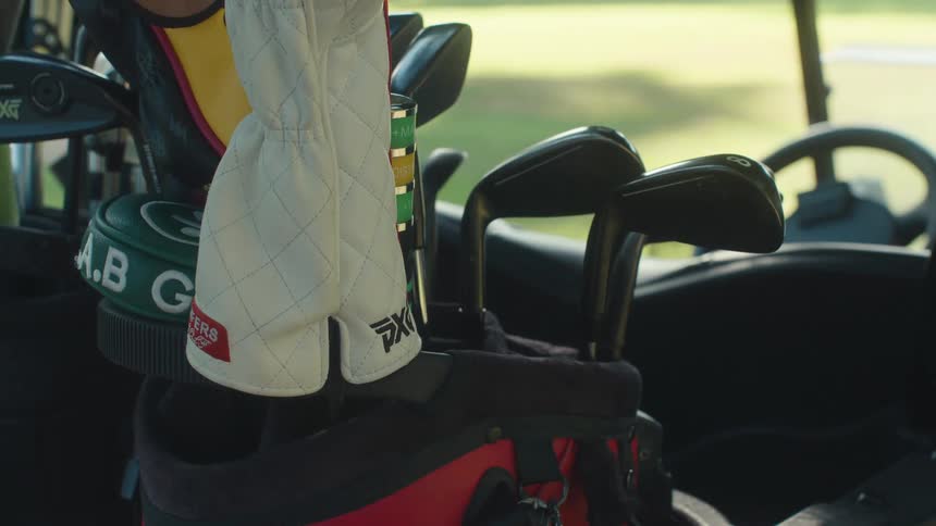 A golfer's hand reaches into a golf bag to select a club while sitting in a cart on a sunny day
