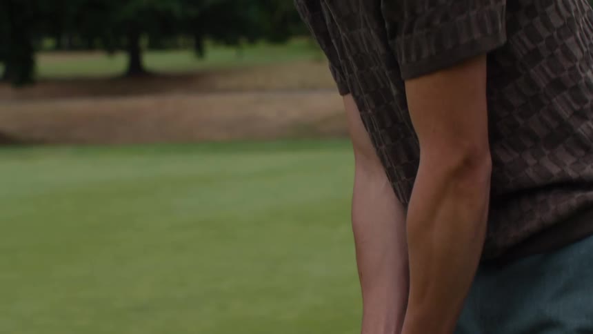 A young male golfer concentrates on his putting form, with the camera slowly tilting up from his hands to his face