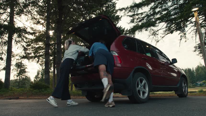 A man and woman unload their golf bags from an SUV in a tree-lined parking lot before a game