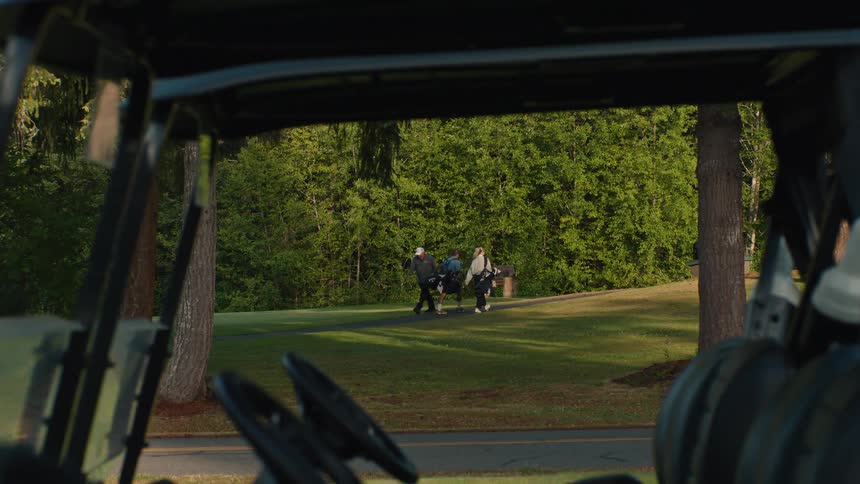 View from inside a golf cart as a group of three golfers walks along a path on a lush green course