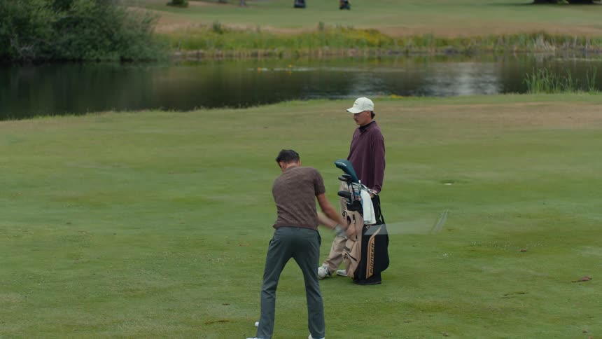 A young golfer takes a powerful swing on the fairway as his companion watches from beside the golf bag