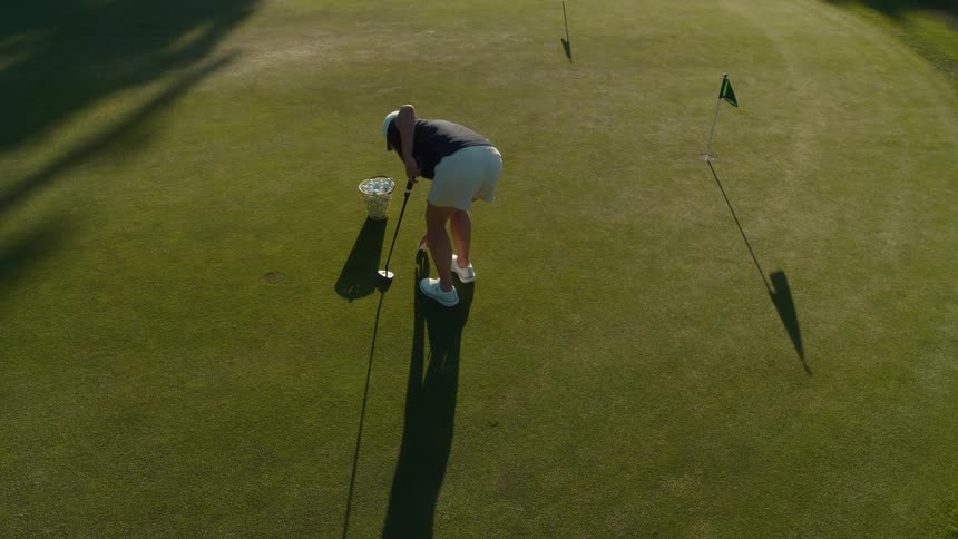 High angle view of a woman practicing putting with a basket of golf balls on a sunny green in slow motion