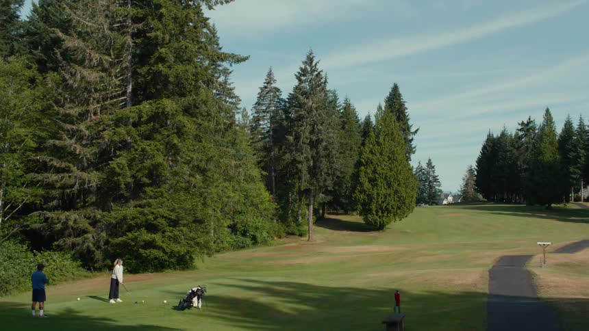 A group of golfers takes turns teeing off on a scenic course surrounded by a dense evergreen forest