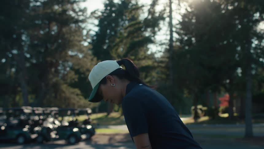 A focused female golfer in a cap prepares for a swing in slow motion at a sunny golf course