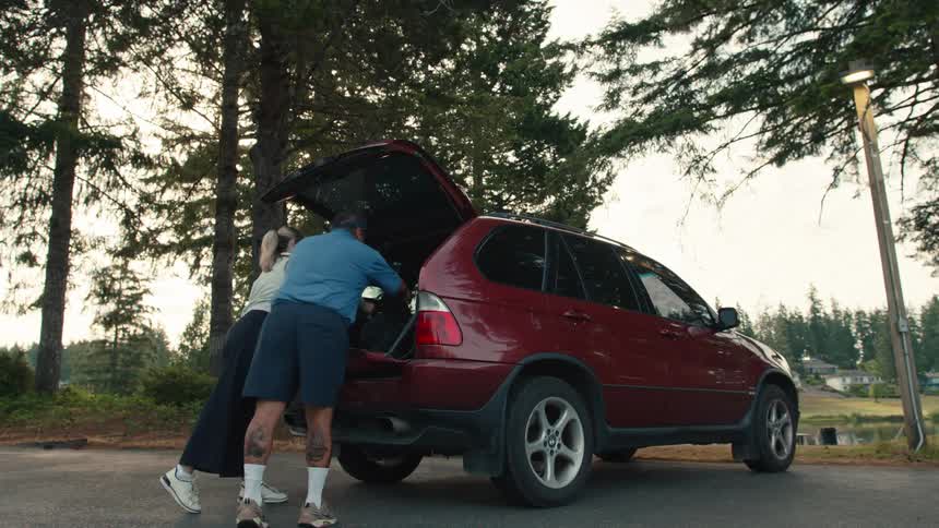 A man and a woman unload their golf bags from the back of their SUV in a parking lot before heading out to play a round