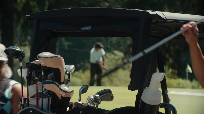 Slow zoom out from a golfer taking a shot on the green, with other players and their carts in the foreground