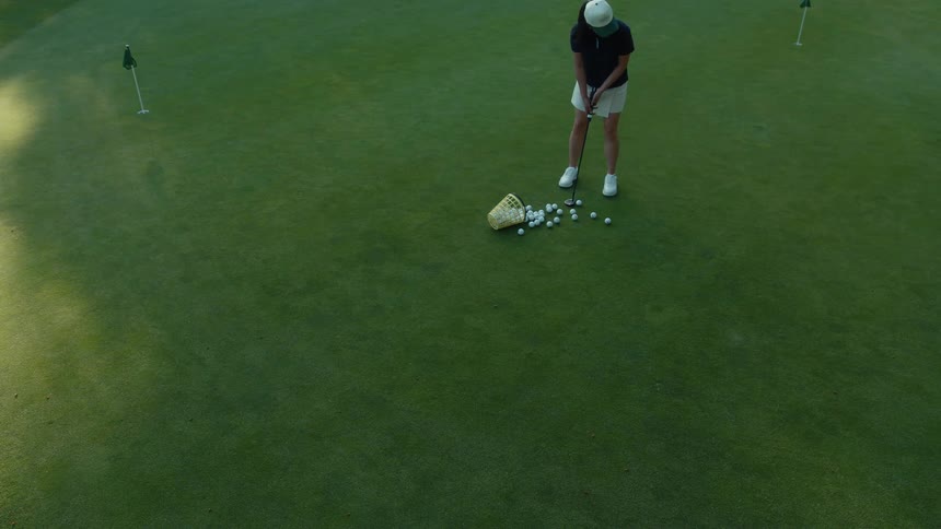 High angle shot of a female golfer walking onto a lush putting green and setting up for a practice session with a basket of balls