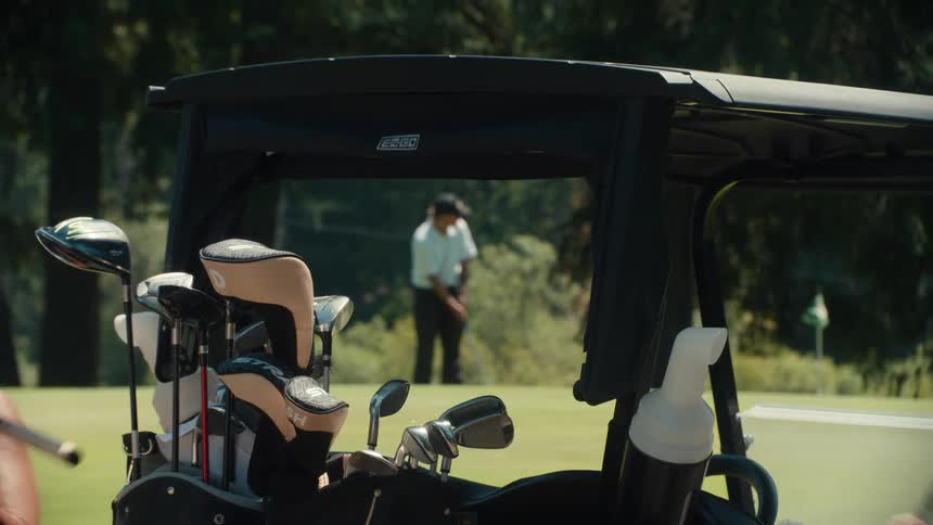 Slow zoom out from a man putting on a golf green to reveal friends waiting in their carts on a sunny day