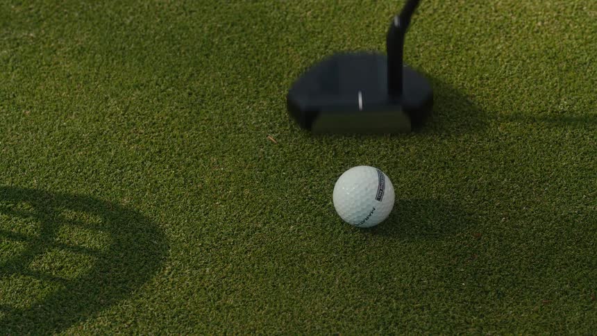 A top-down slow-motion view shows a golfer practicing their putt and adjusting the ball with their shoe on a vibrant green
