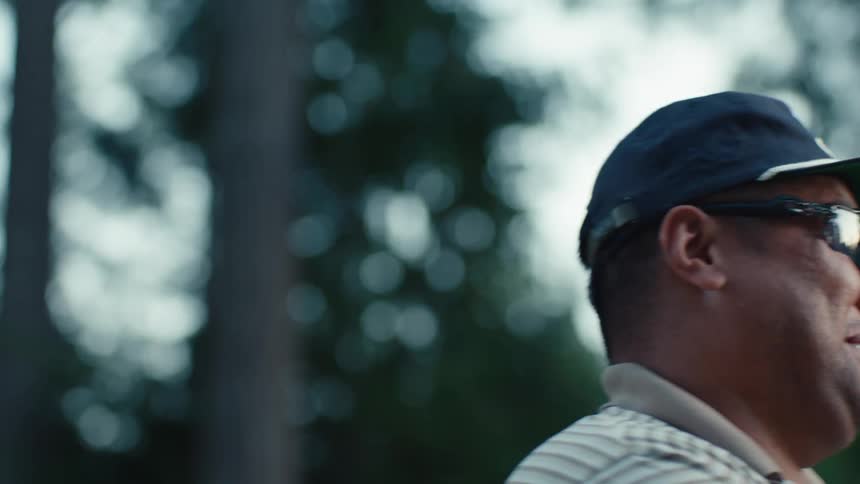 Slow motion close up of a man in sunglasses and a hat smiling and laughing while having a casual conversation outdoors