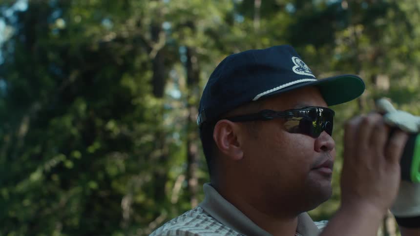 A male golfer wearing sunglasses uses a rangefinder to check the distance before his next shot