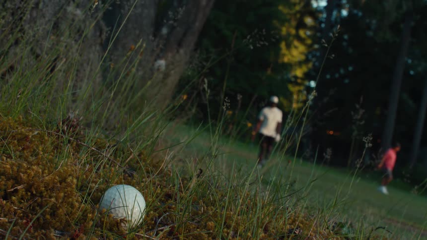 A close-up of a lost golf ball in the grassy rough as a man approaches to take his next shot on the course