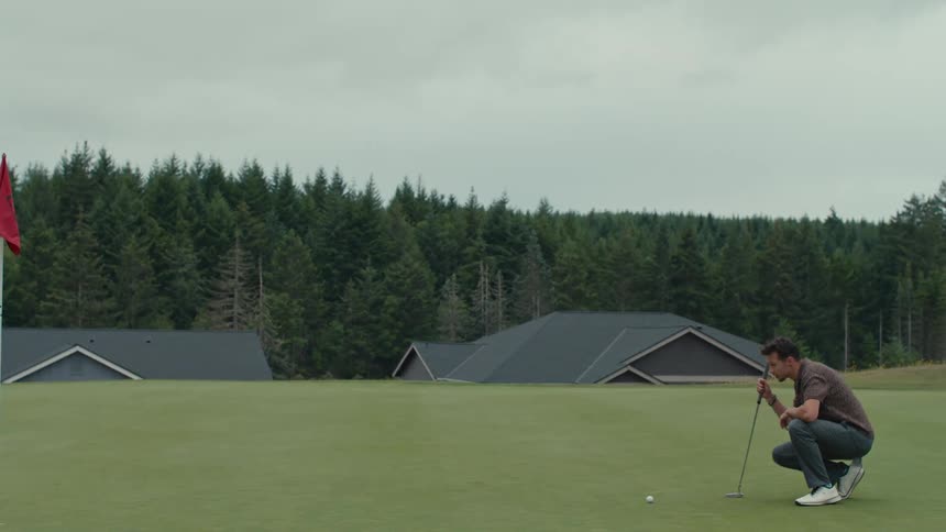Two friends walk onto a beautiful golf course where one player lines up his shot and prepares to putt on the green
