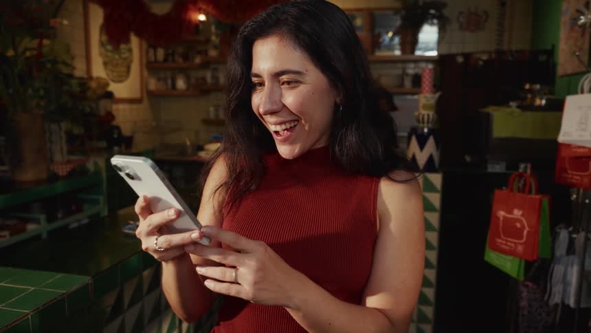 Cinemagraph of an excited woman reacting with a huge smile to something she sees on her smartphone in a shop