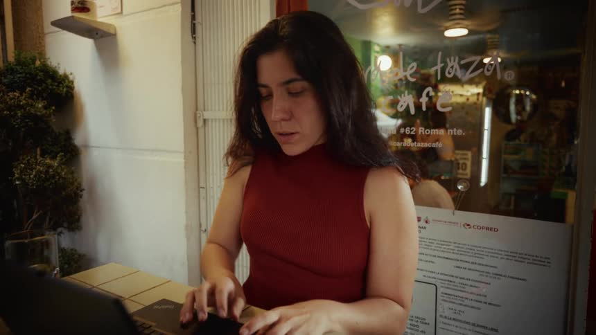 A young woman opens her laptop to start working while sitting at an outdoor table at a sidewalk cafe