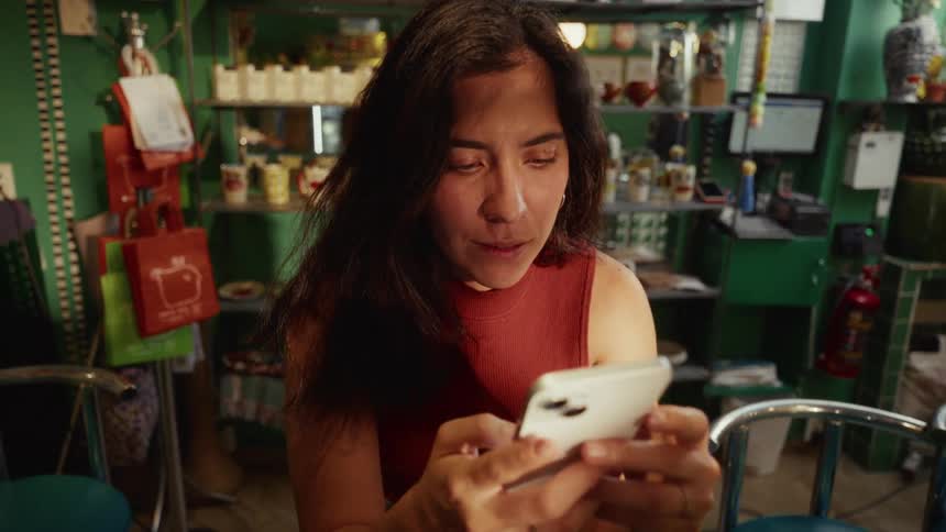 Slow zoom in on a woman smiling as she uses her phone while sitting at a counter in a unique shop