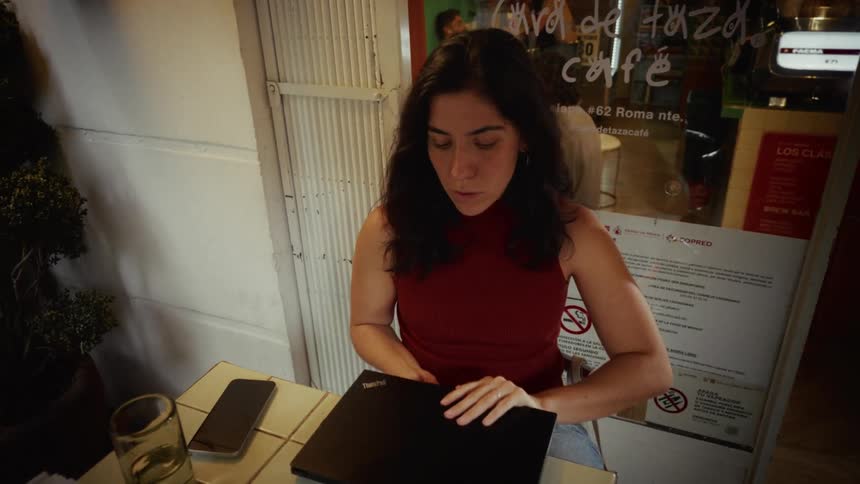 A woman sits at an outdoor cafe table and takes her laptop out of a case to begin working in slow motion