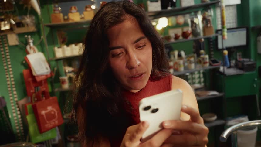 A female small business owner smiles warmly while looking at her smartphone in her eclectic shop