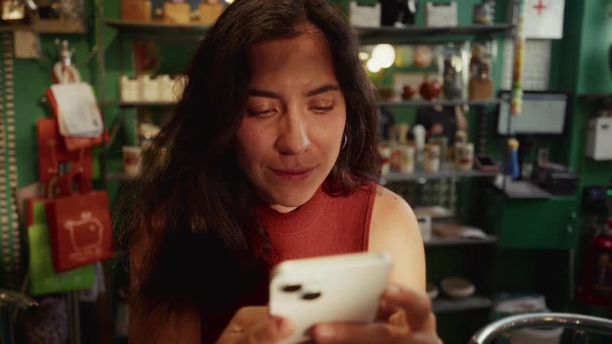 A happy woman smiles while looking at her smartphone inside a cozy, eclectic shop