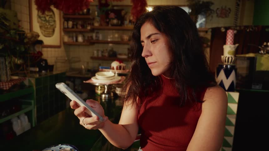 A young woman in a colorful vintage cafe smiles while looking at her smartphone