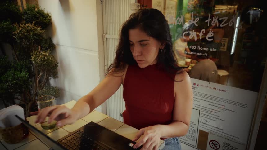 A focused woman opens her laptop and begins working at a small outdoor table at a cafe