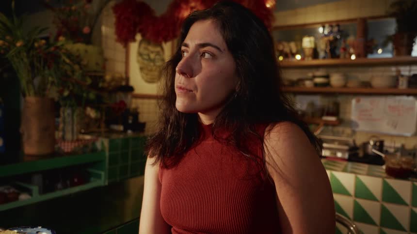 A woman in a quirky cafe reads something on her phone and then looks away with a pensive expression