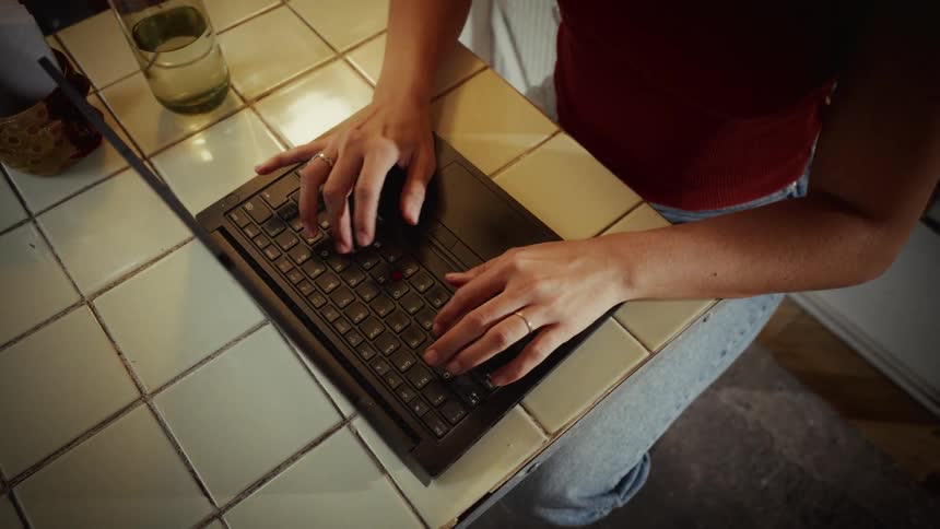 Top-down perspective of a female freelancer typing on her laptop computer while sitting at a tiled desk